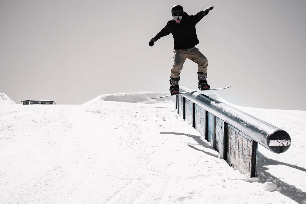 Snowboardzista ześlizguje się po metalowej poręczy w snowparku