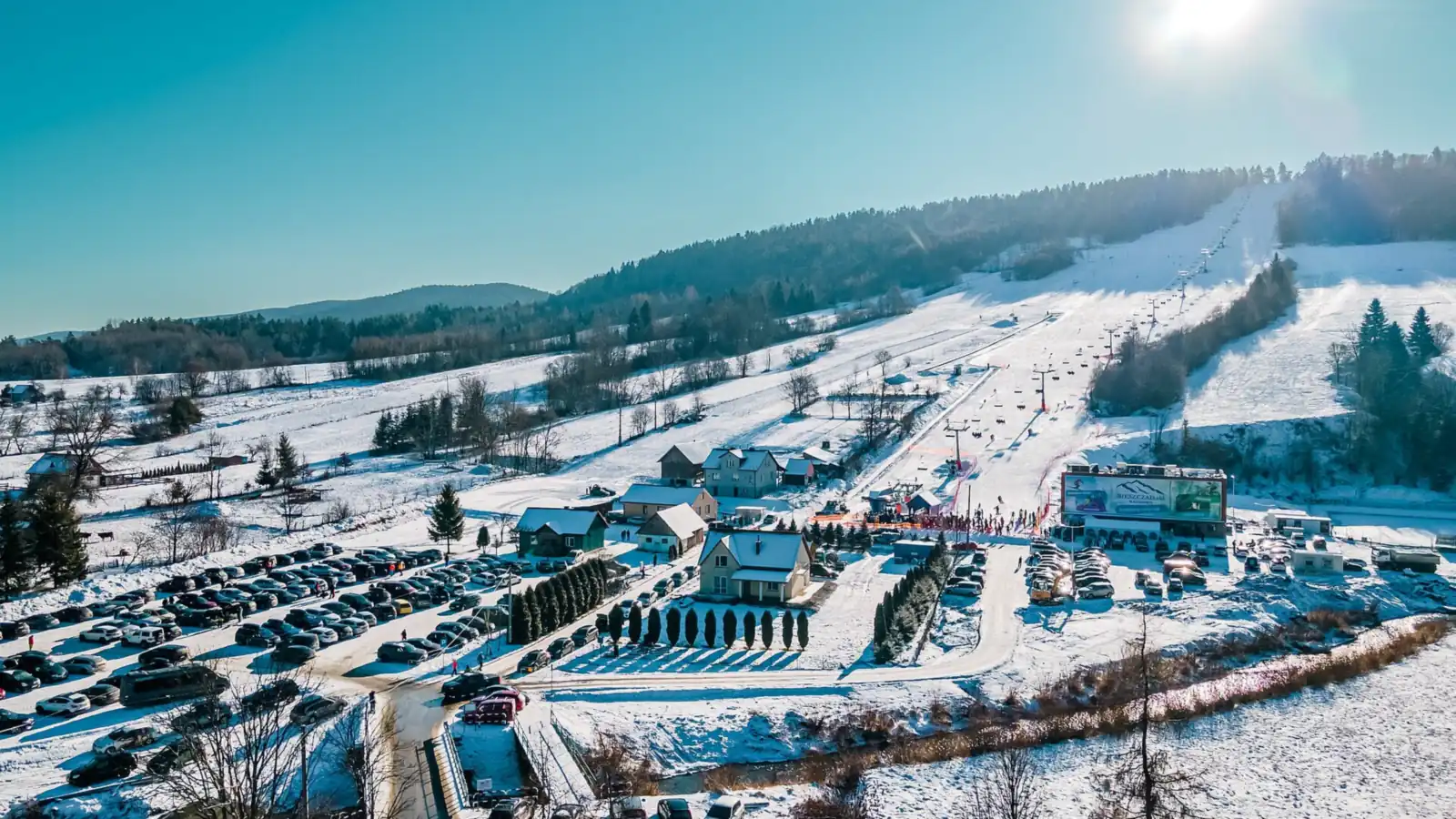 Widok z lotu ptaka na ośnieżone trasy stacji Bieszczad.ski w Wańkowej, parking i budynki u podnóża