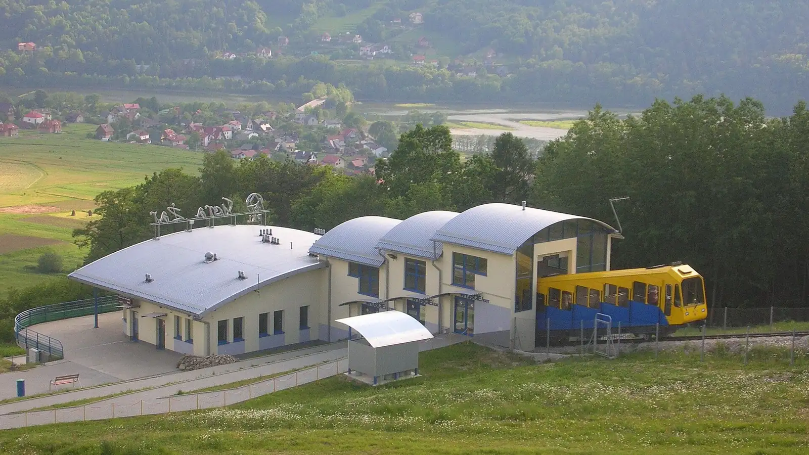 Górna stacja kolei linowo-terenowej na Górze Żar z żółtym wagonikiem, w dole dolina Soły