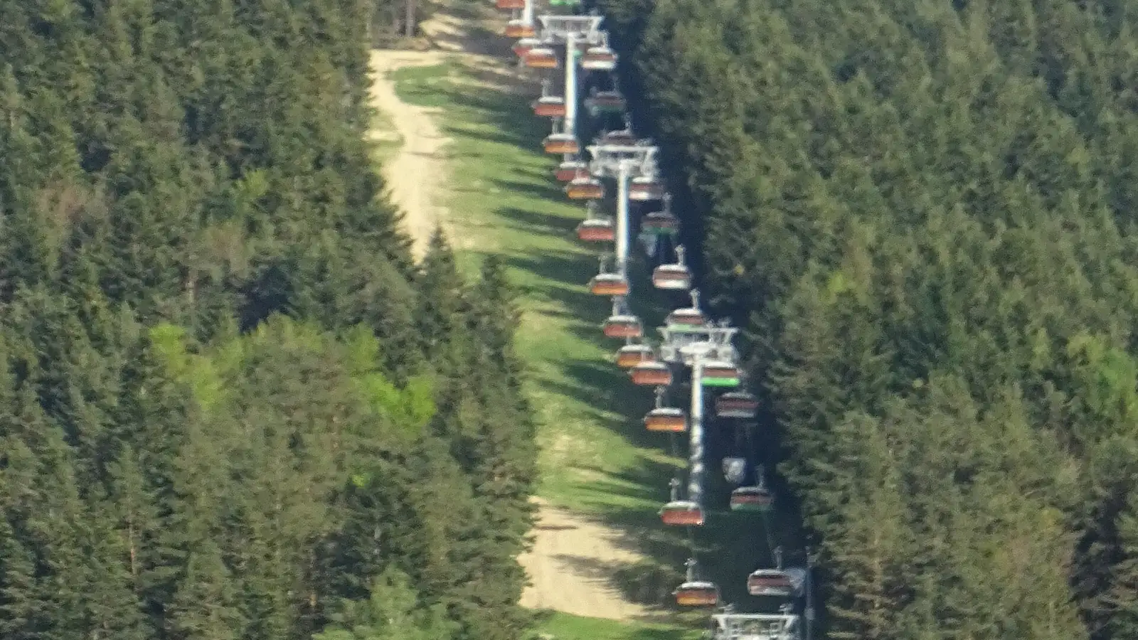 Kolej krzesełkowa biegnąca przecinką w gęstym lesie na stoku Kasina Ski latem, widok z góry