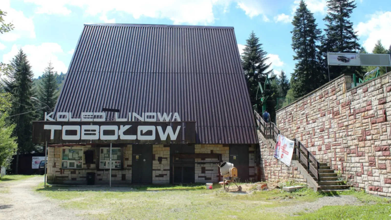 Budynek stacji z napisem Kolej Linowa Tobołów w otoczeniu świerków latem