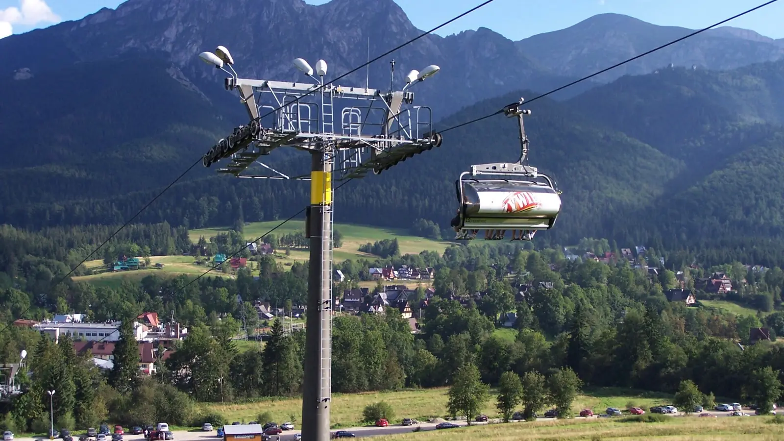 Słup kolei krzesełkowej z kanapą nad Zakopanem, w tle masyw Giewontu i Tatry latem