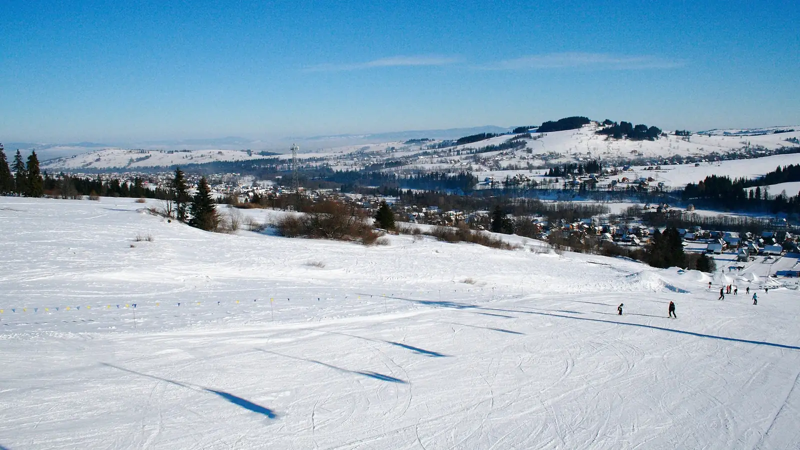 Szeroka ośnieżona trasa Witów-Ski w słońcu, w tle dolina i pagórki Podhala pod błękitnym niebem