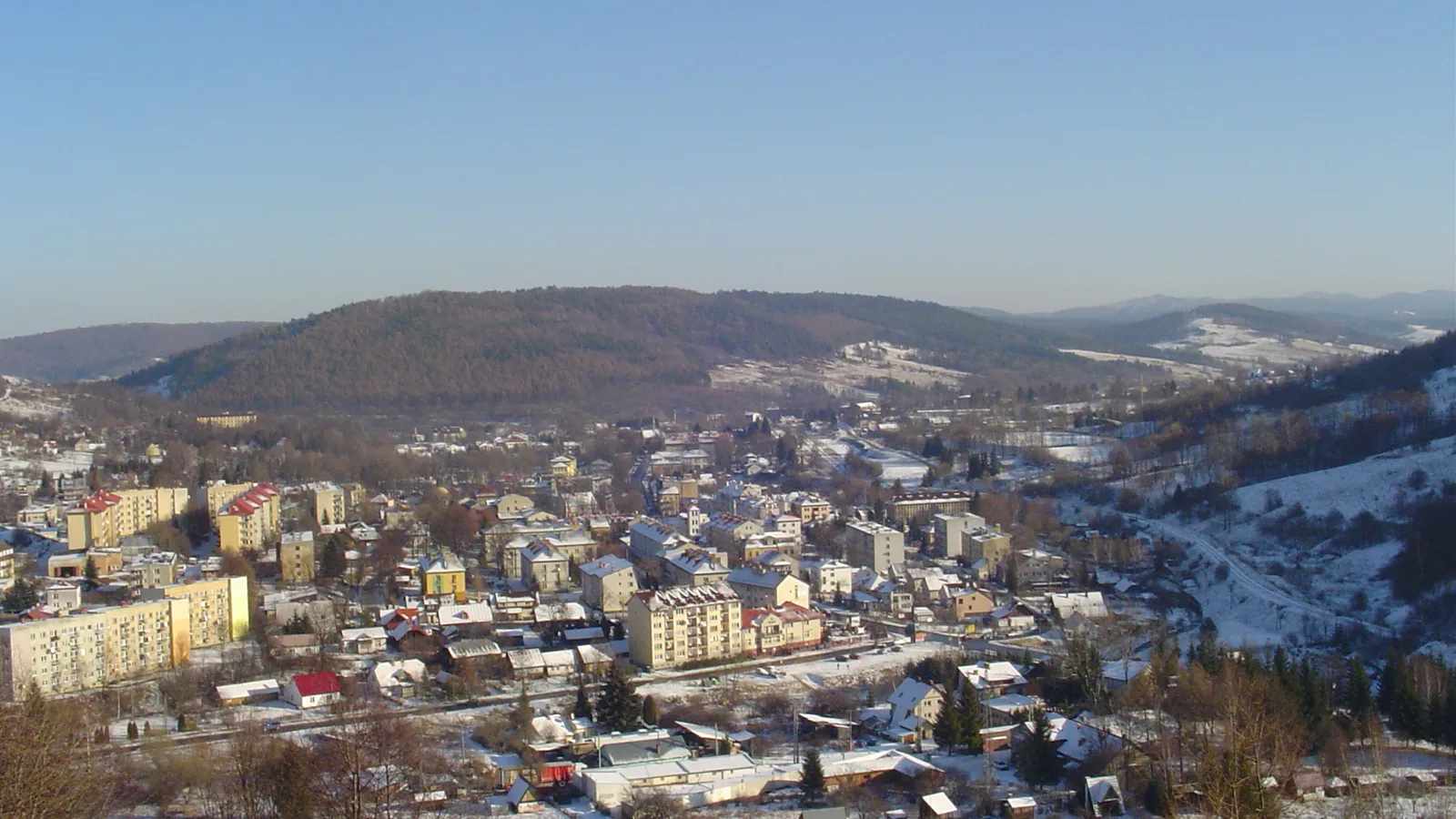 Zimowa panorama Ustrzyk Dolnych z blokami i domami w dolinie, w tle zalesione wzgórza Bieszczadów