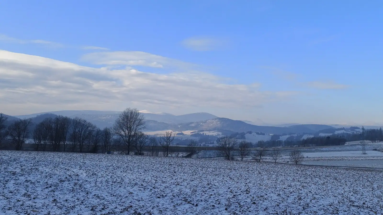 Ośnieżone pasmo Sudetów ze Śnieżką na horyzoncie pod błękitnym niebem