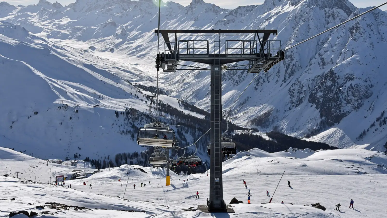 Podpora kolei krzesełkowej nad ośnieżonym stokiem, w tle zaśnieżone pasmo gór Silvretta