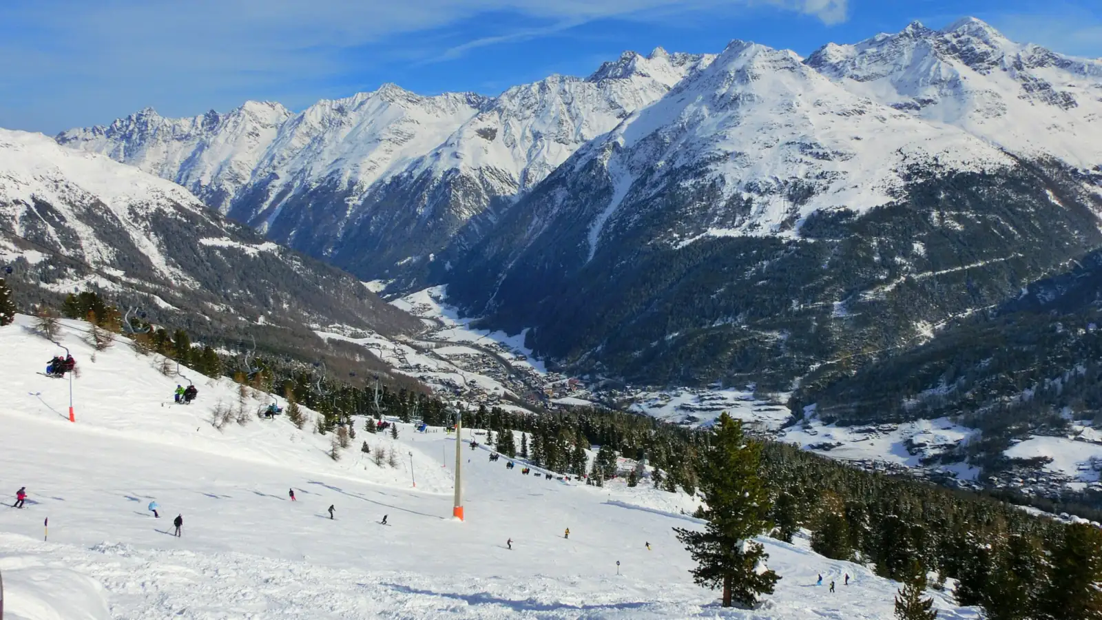 Szeroki ośnieżony stok z narciarzami nad doliną Ötztal, w tle zaśnieżone szczyty Alp