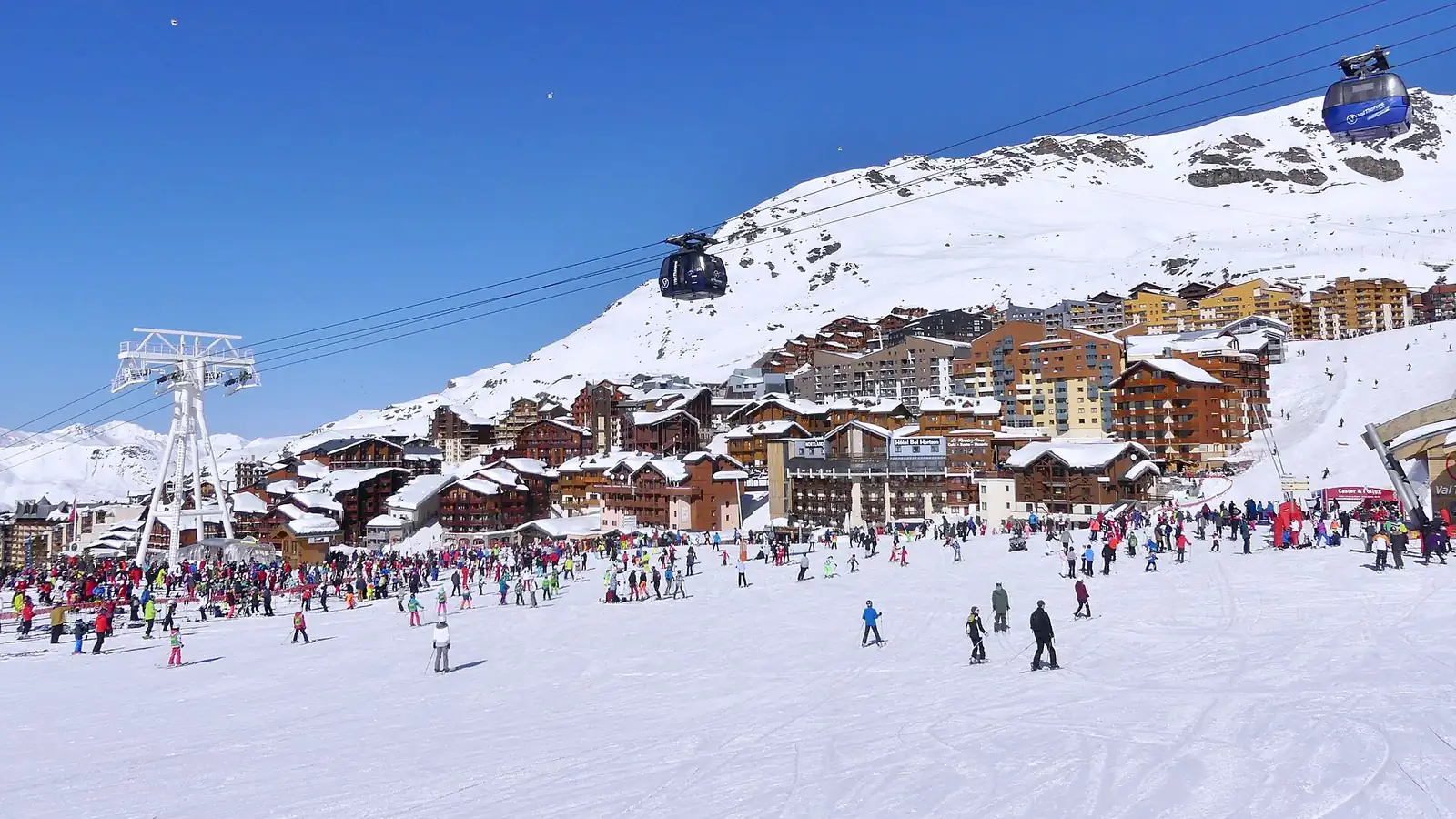 Narciarze u podnóża tras w Val Thorens, nad nimi zabudowa ośrodka i kolej gondolowa na ośnieżonym zboczu