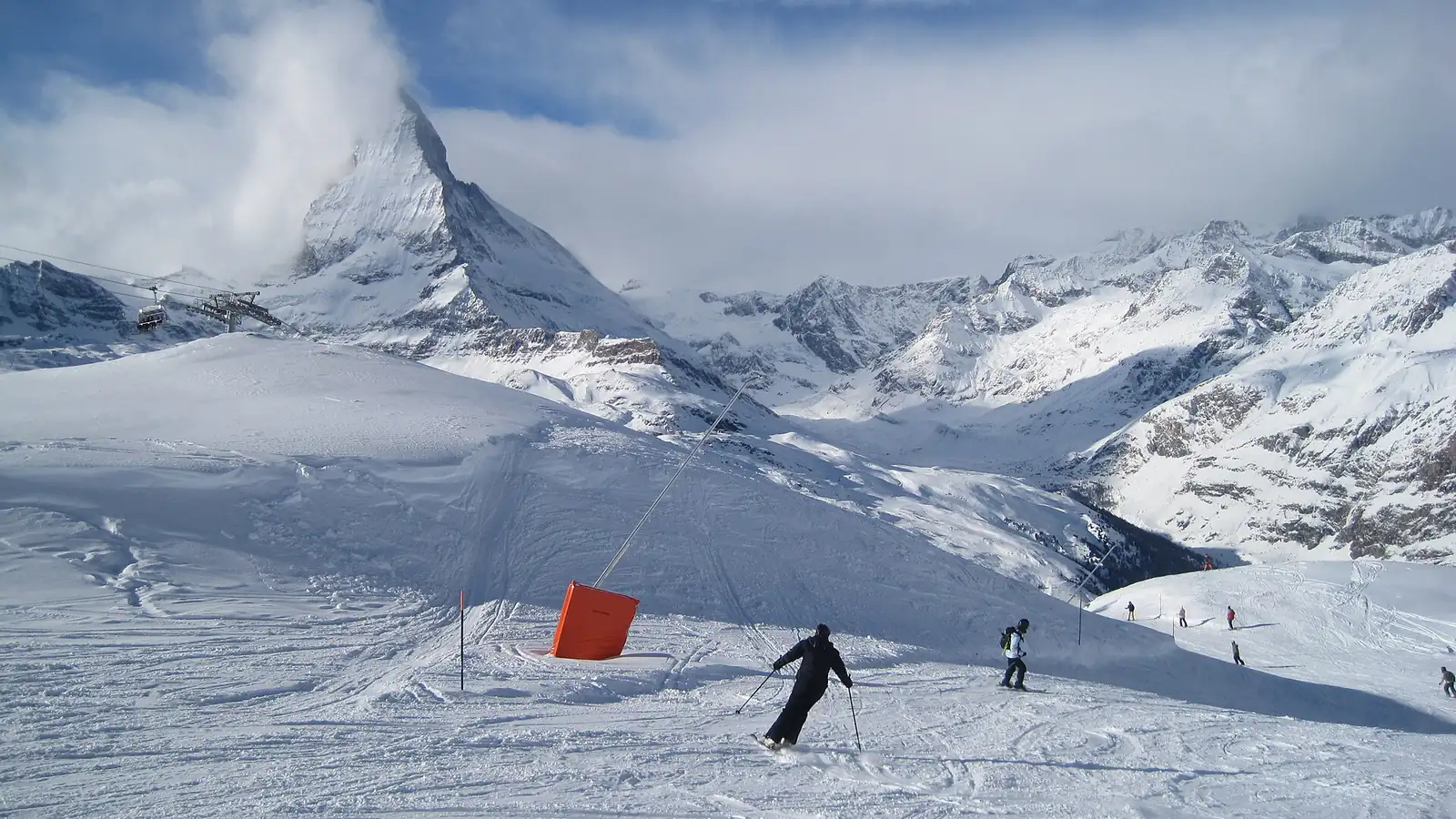 Narciarze na ośnieżonej trasie na Gornergrat nad Zermatt, w tle ostra piramida Matterhornu w chmurach