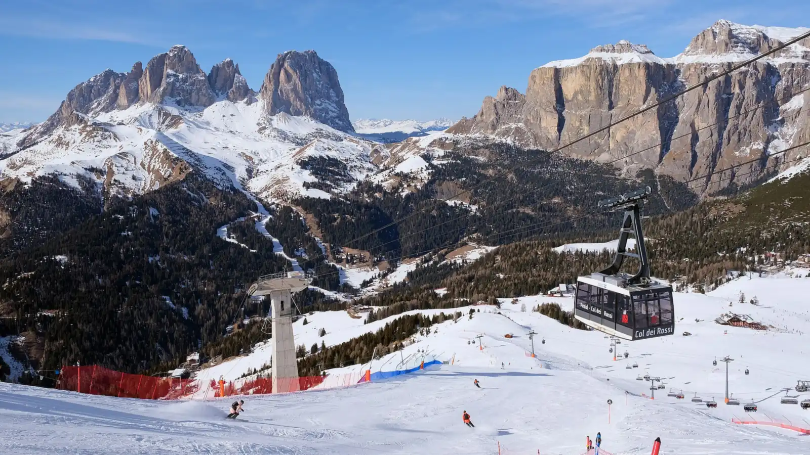 Wagonik kolei linowej nad ośnieżonymi trasami, w tle turnie Sassolungo i ściany masywu Sella w Dolomitach