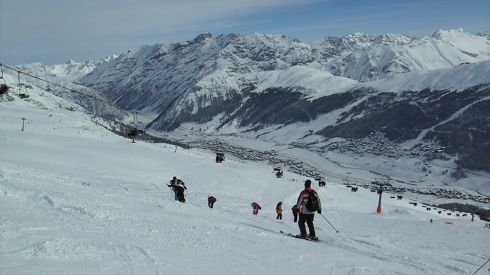 Narciarze na szerokim stoku nad doliną Livigno, w tle ośnieżone grzbiety gór i wyciągi